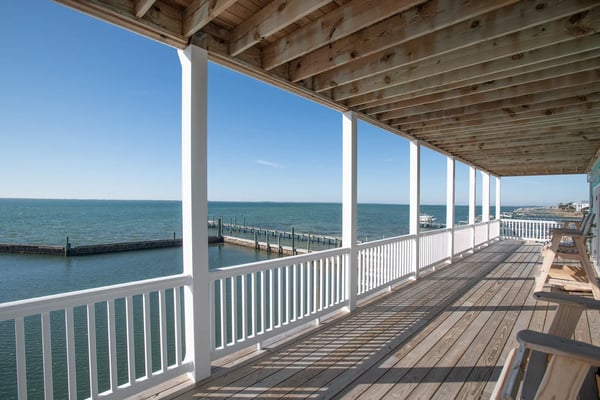 Covered waterfront deck with white railings, wooden beams, and ocean views with pier pilings below